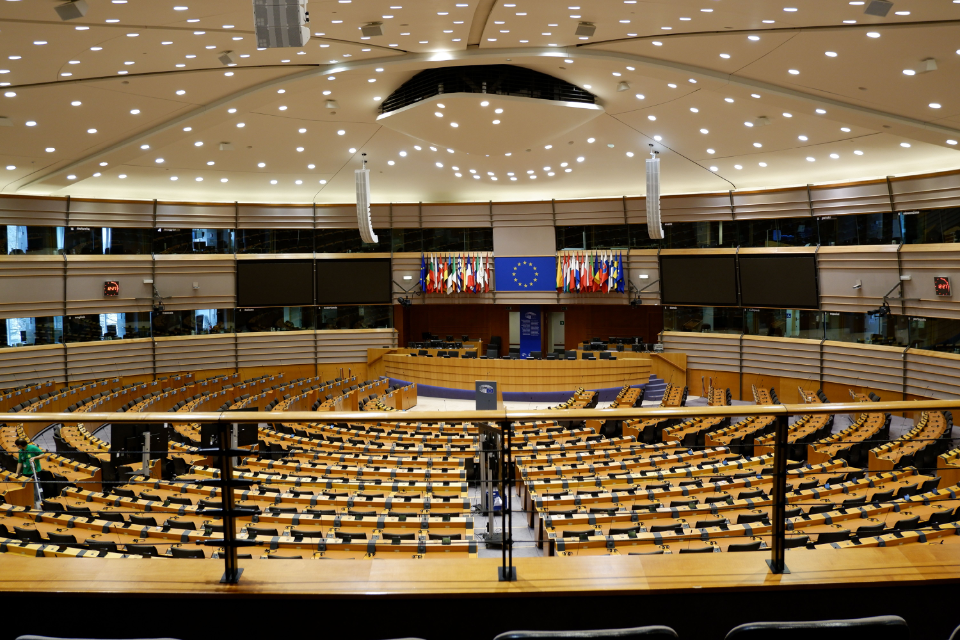 Vue d'ensemble d'une assemblée vide au Parlement européen, avec des rangées de sièges pour les députés et un drapeau de l'Union européenne.