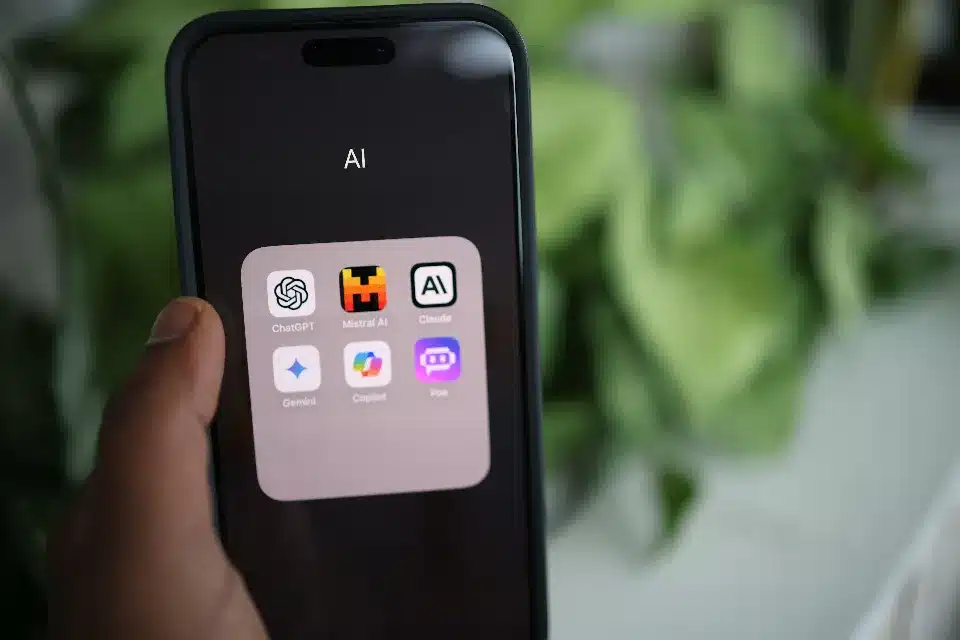 Un smartphone affiche une grille d'applications d'IA dont ChatGPT, Mistral AI, Claude, Gemini, Copilot et Poe.
