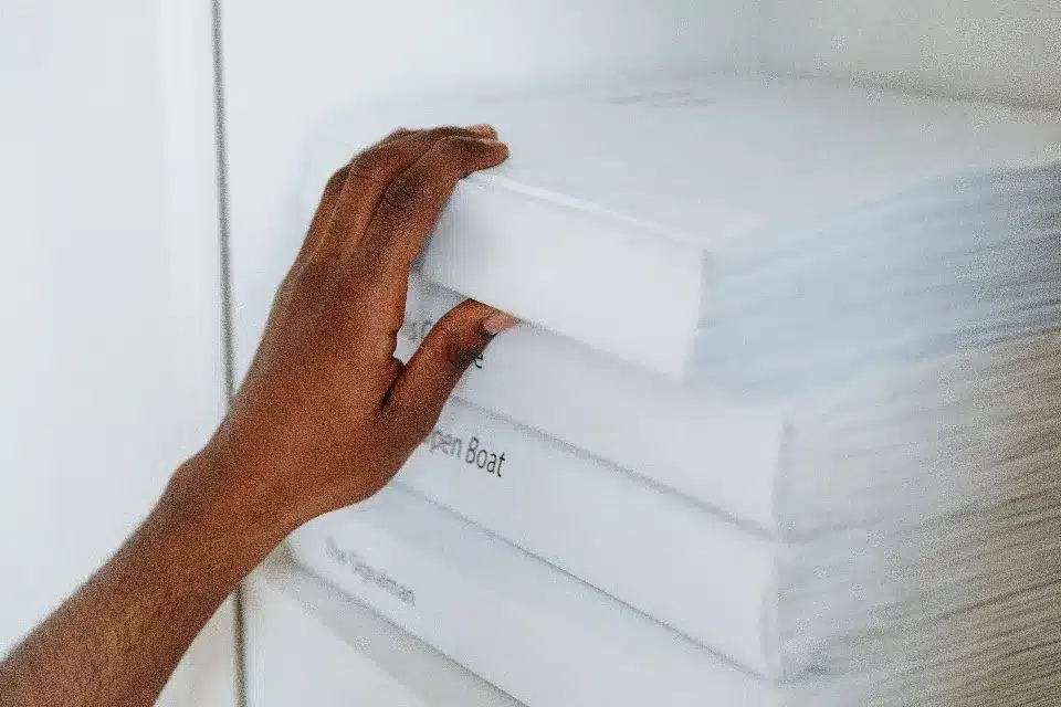 main-qui-selectionne-un-livre Une main attrape le premier livre blanc d'une pile de livres blancs, révélant le titre 'The Ingolman' sur le livre du dessous.