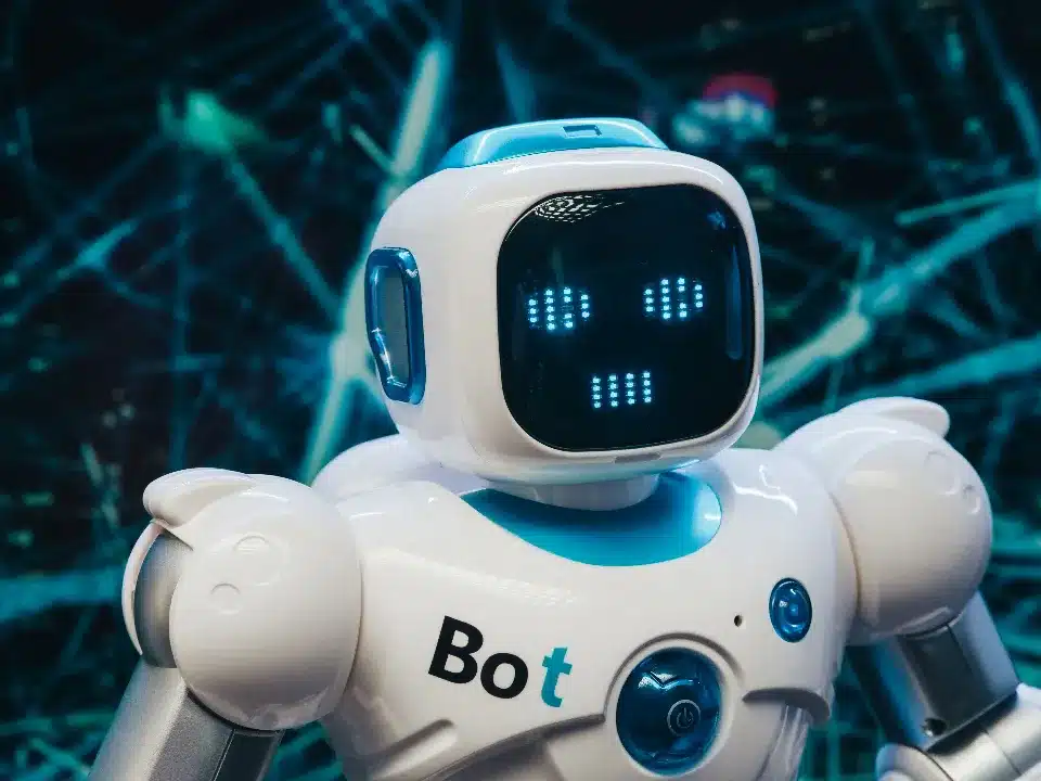 Gros plan sur un petit robot blanc et bleu avec des lumières bleues sur son écran, le mot "Bot" est écrit sur son torse.